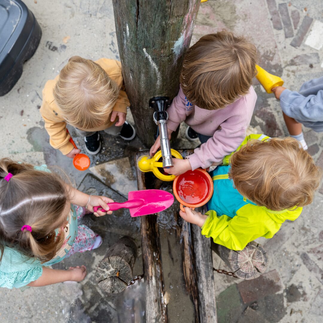 Vier kleuters spelen met bij een kraan met water, bakjes, schepjes,